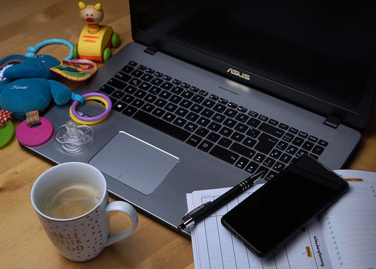 Open Asus laptop covered with baby toys, a calendar, a cellphone. In the foreground is a coffee mug with the words "Sparkle wherever you go"